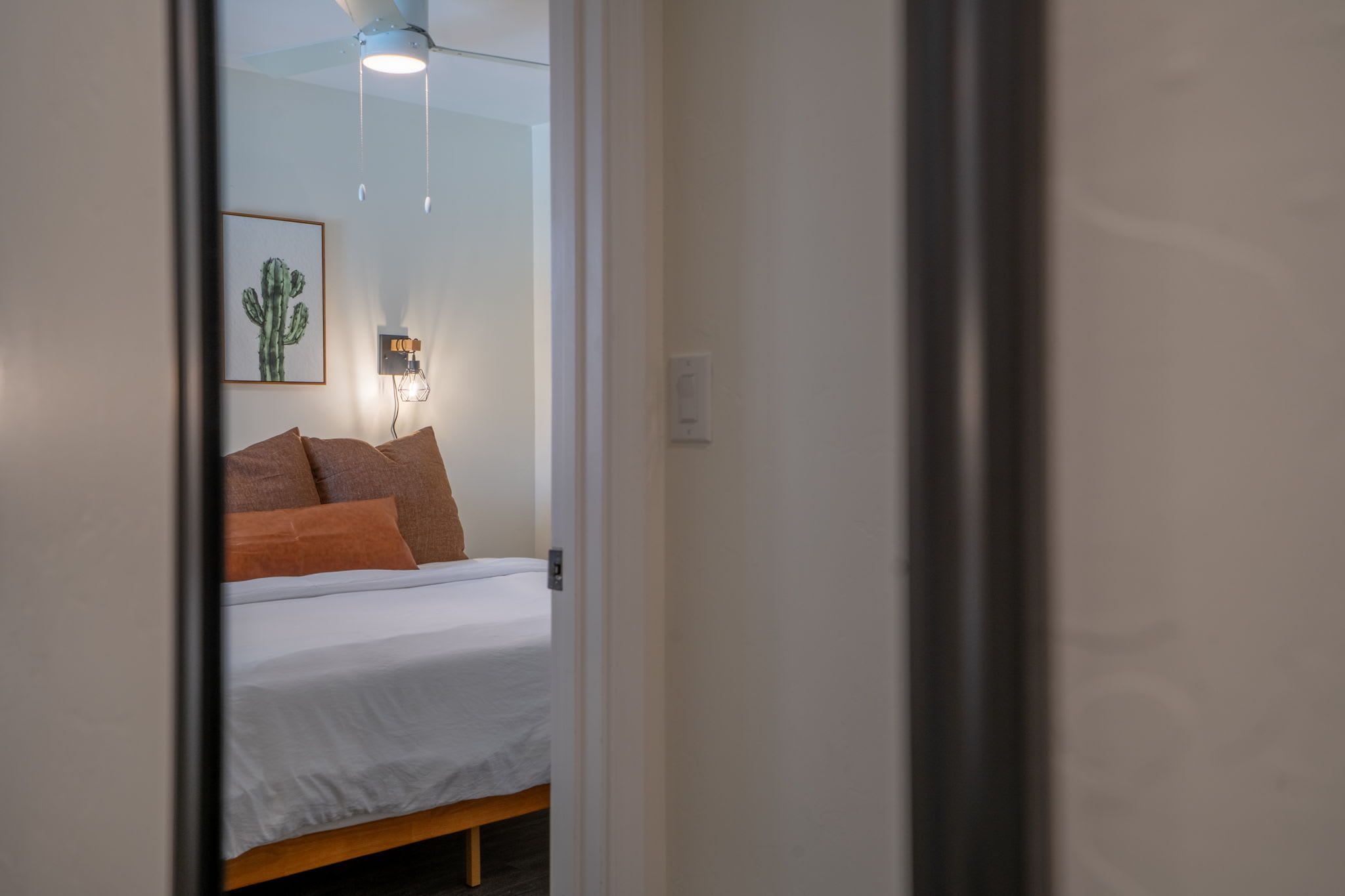 A bedroom with a bed, pillows, a wall-mounted light fixture, and a ceiling fan.