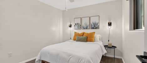 A bedroom with a bed, a ceiling fan, wall-mounted lights, and a window.