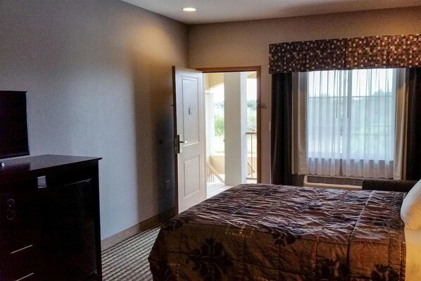 A hotel room with a bed, a dresser, a television, and a window with curtains. - Functional Studio Offers Extended Stay Comfort Near Downtown Beeville (Beeville)
