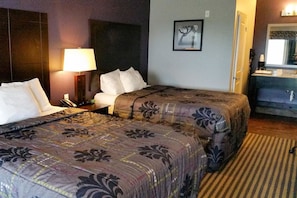 A hotel room with two beds, a bedside table with a lamp, a mirror, and a bathroom with a sink and mirror. - Studio w/ Kitchenette & Space for Pets Near Coastal Bend College (Beeville)