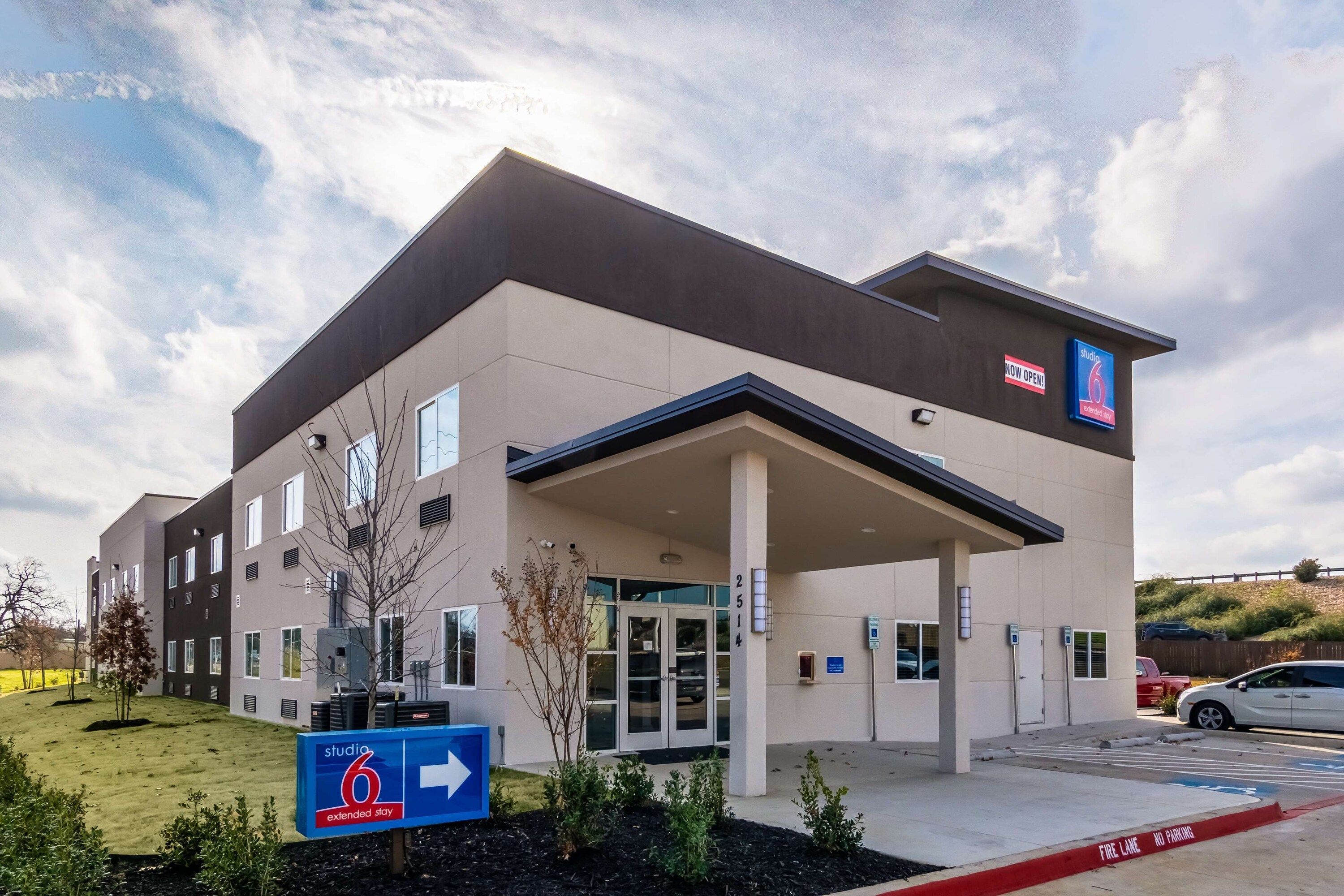 A modern hotel with a flat roof, a covered entrance, and a sign indicating Studio 6.
