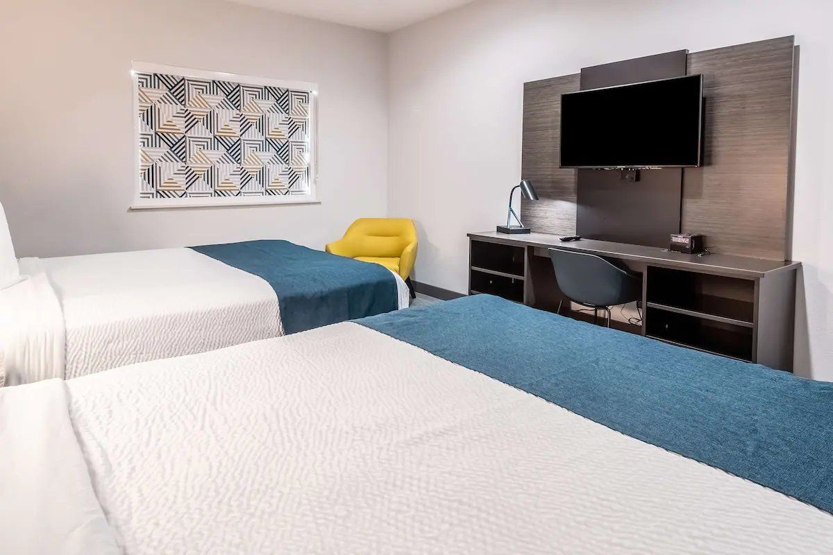 A hotel room with two beds, a desk, a chair, a TV, and a patterned wall art.