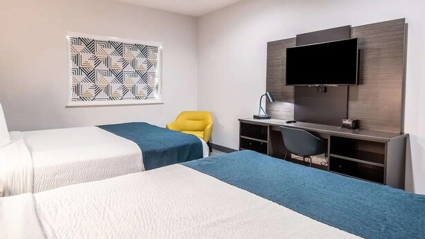Ein Hotelzimmer mit zwei Betten, einem Schreibtisch, einem Stuhl, einem Fernseher und Wandbild mit Muster.