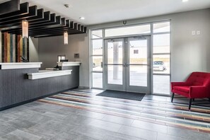 Et receptionsområde med moderne design, der inkluderer en receptionsdisk, en rød stol og en stor glasdør, der fører udendørs.
