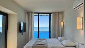 Une chambre d’hôtel avec un lit, une télévision, une fenêtre avec des rideaux et une vue sur la mer.