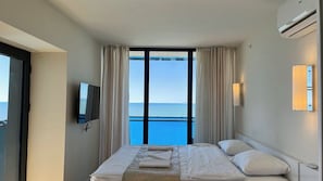 Une chambre d’hôtel avec un lit, une télévision, une fenêtre avec des rideaux et une vue sur la mer.