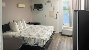 Habitació d'hotel amb llit, taula de nit, escriptori petit, cadira, finestra amb cortines i porta amb un avís.