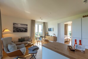 A modern living room with a sofa, armchair, and a dining area with a table and chairs. - Sea and Sky Pellworm—Exclusive Penthouse with a 300° View of the Wadden Sea (Pellworm)