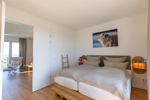 Quarto com cama grande, escada de madeira, cadeira e um quadro na parede.