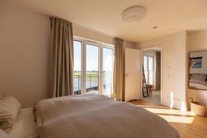 A bedroom with a large bed, a view of a balcony, and a door leading to another room. - Sea and Sky Pellworm—Exclusive Penthouse with a 300° View of the Wadden Sea (Pellworm)
