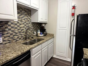 A kitchen with white cabinets, a granite countertop, a stainless steel sink, a coffee maker, and a black refrigerator. - 500 Yds to AT&T Stadium Balcony 2BR Sleeps 6 (Arlington)