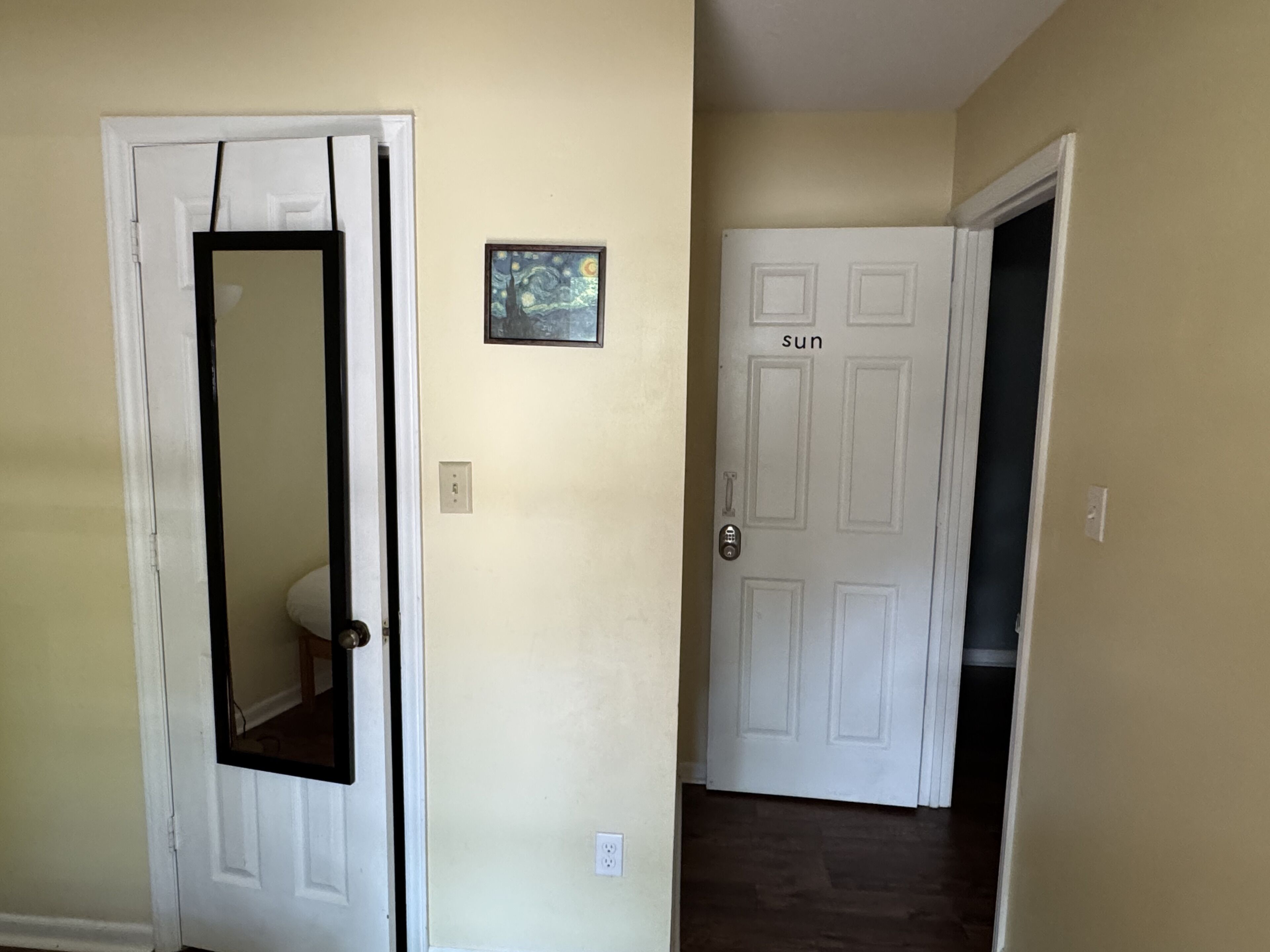 A hallway with a white door on the left, a small framed picture on the wall, and a door labeled 'sun' on the right.