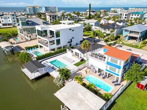 A modern hotel with a pool, waterfront views, and a mix of residential and commercial buildings in the background. - Vida Isla on Palermo- Heated Pool- Sleeps 10 (Fort Myers Beach)