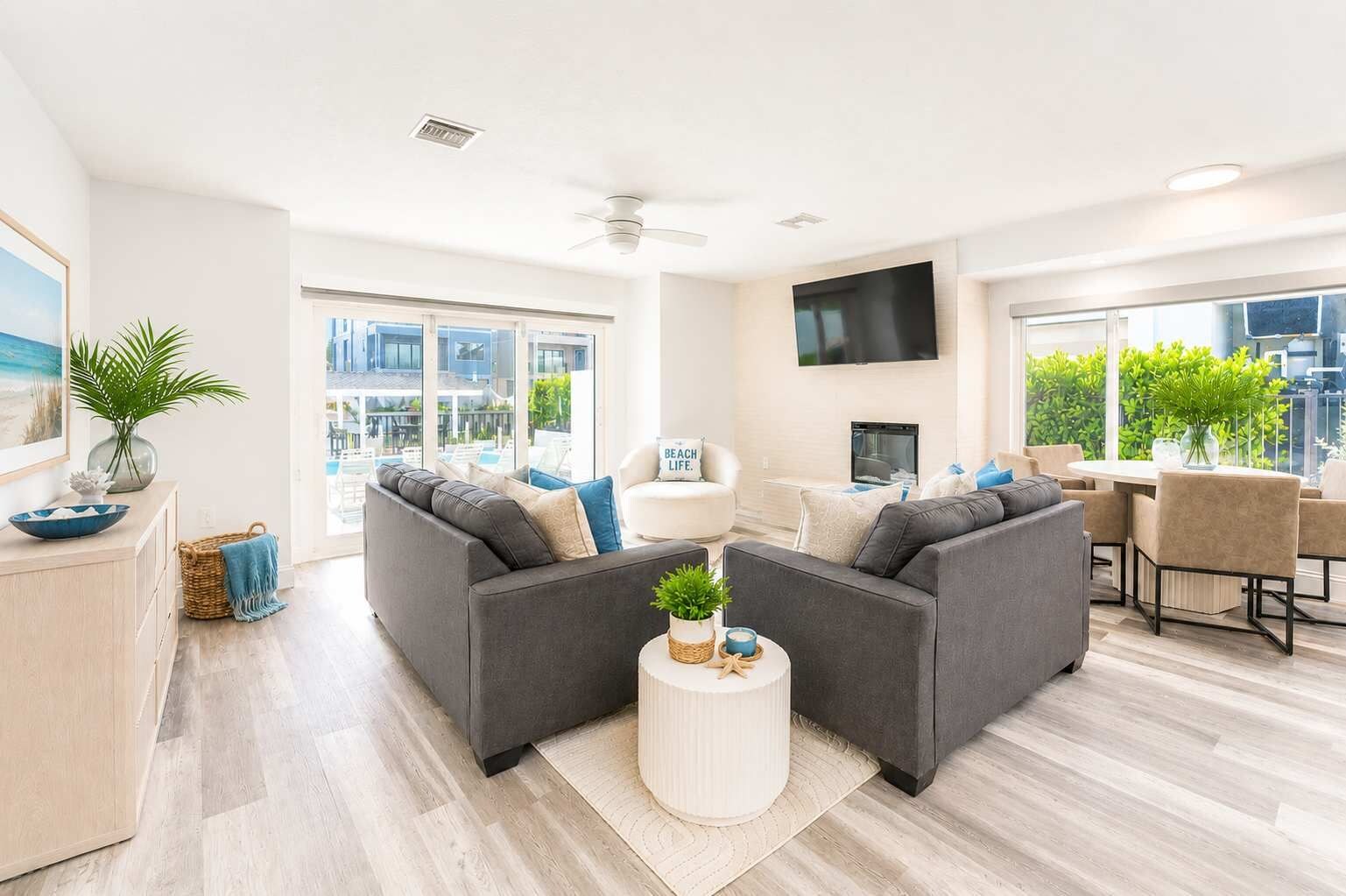 A modern living room with grey sofas, a flat-screen TV, and a dining area with a table and chairs.