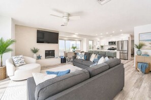 A modern living room with a grey sofa, a white armchair, and a flat-screen TV mounted on the wall. - Vida Isla on Palermo- Heated Pool- Sleeps 10 (Fort Myers Beach)