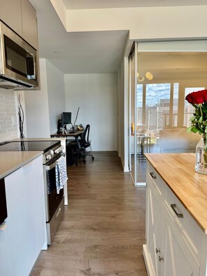 A modern kitchen with a microwave, stove, and wooden flooring. - Fully furnished condo in King West, perfect for 30+ night stays (Toronto)