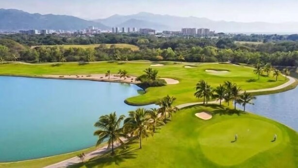 A golf course with a lake, palm trees, and a cityscape in the background. - Luxury Golf and Family getaway, Vidanta Nuevo Nayarit, Beachfront resort (Nuevo Nayarit)