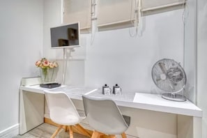 A modern office space with a white desk, two chairs, a computer monitor, a fan, and a vase with flowers. - 18-square-meter studio apartment - Bir-Hakeim / 10 minutes from the Eiffel Tower (Paris)