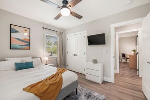 Ein Schlafzimmer mit Bett, Schreibtisch, Fernseher und Deckenventilator.