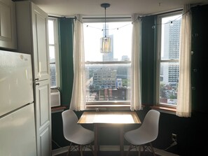 A room with a table and two chairs, a window with curtains, and a view of buildings outside. - Cozy & Quiet 1 Bed/1 Bath Rittenhouse Condo (Philadelphia)