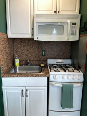 A kitchen with white cabinets, a stainless steel sink, a microwave, and a gas stove. - Cozy & Quiet 1 Bed/1 Bath Rittenhouse Condo (Philadelphia)