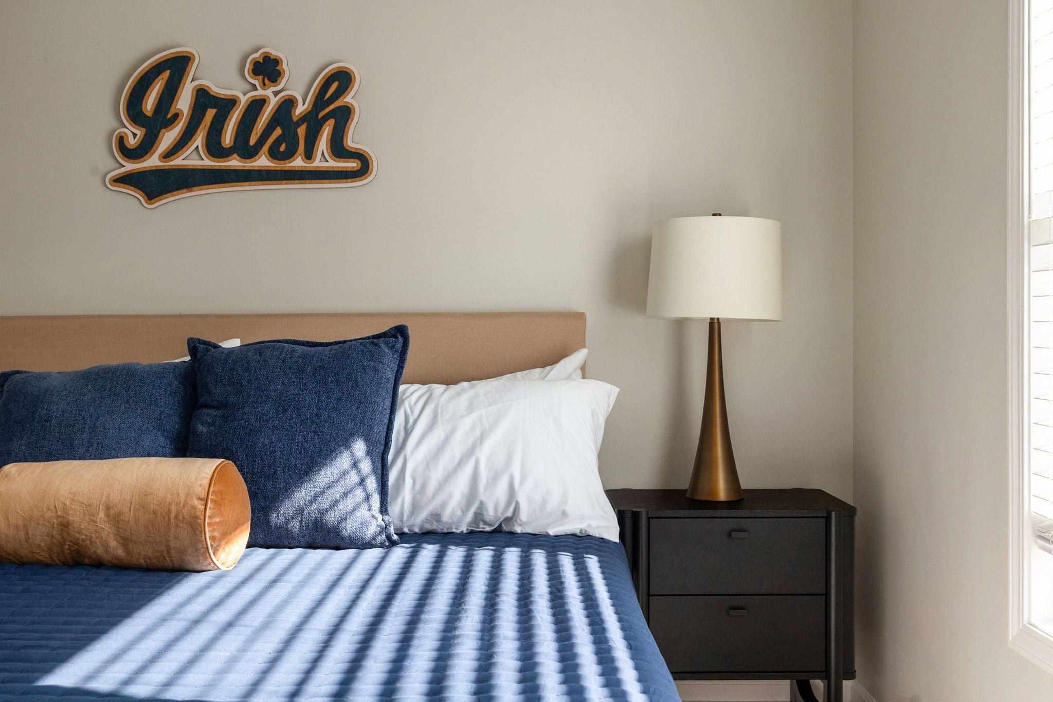 Ein ordentlich bezogenes Bett mit blauer Bettwäsche, einem Holz-Kopfschild und einem an der Wand befestigten Schild mit der Aufschrift 'Irish'.