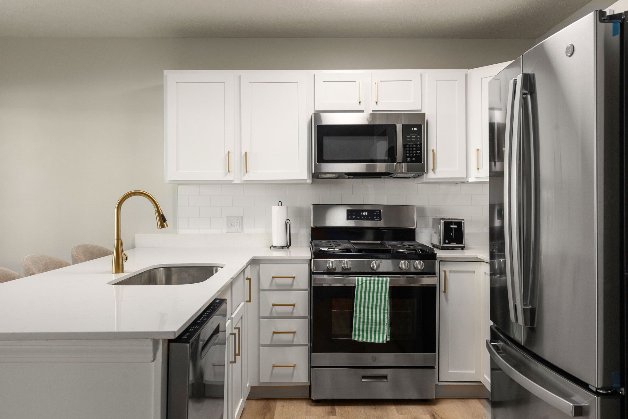 Una cocina moderna con electrodomésticos de acero inoxidable, armarios blancos y un grifo dorado.
