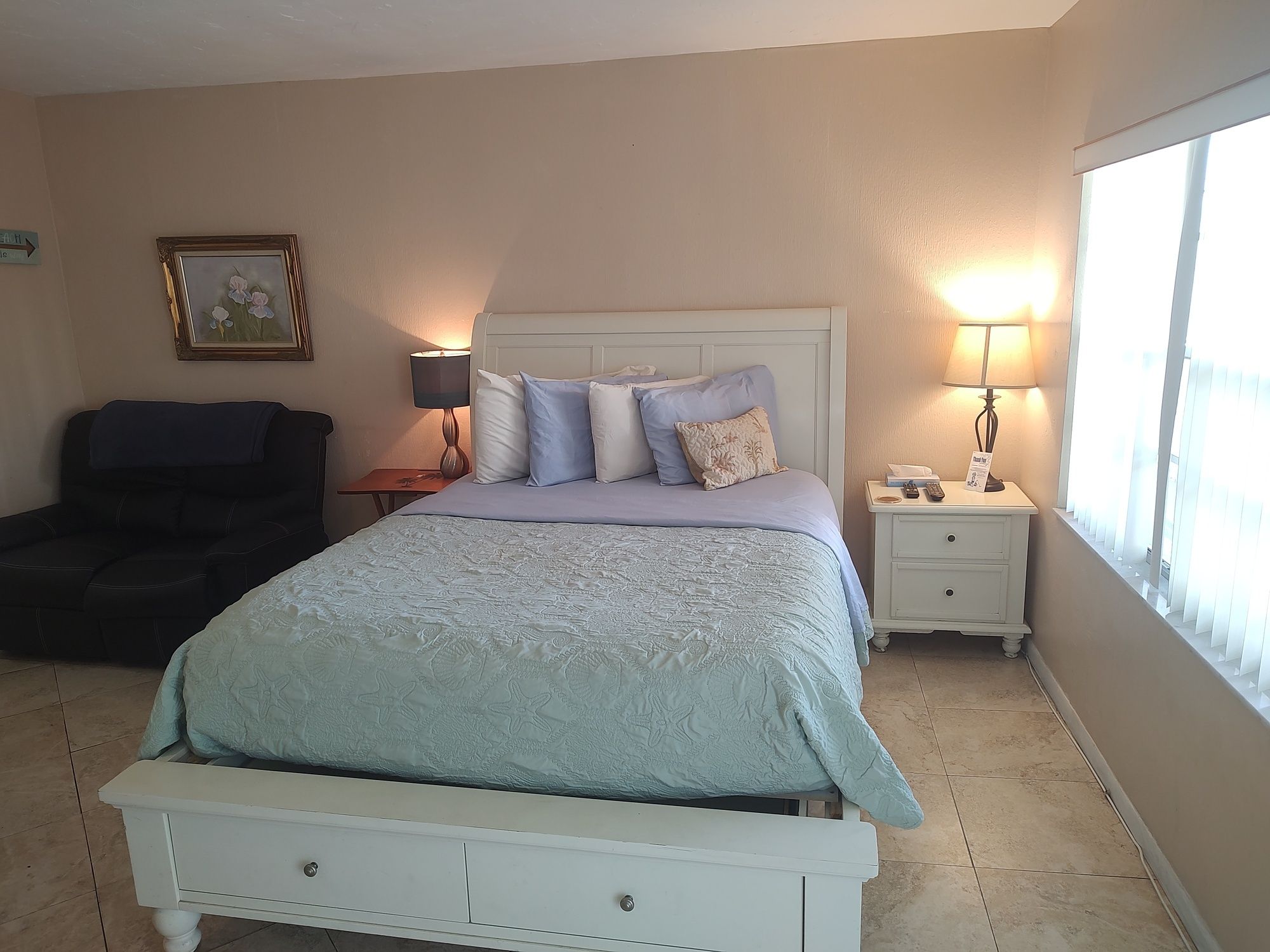 A bedroom with a bed, bedside tables, a nightstand, a lamp, a framed picture, and a chair.