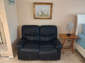 Ein schwarzes Sofa mit weißer Steppung, ein kleiner Holztisch mit einer Lampe und ein gerahmtes Bild an der Wand.