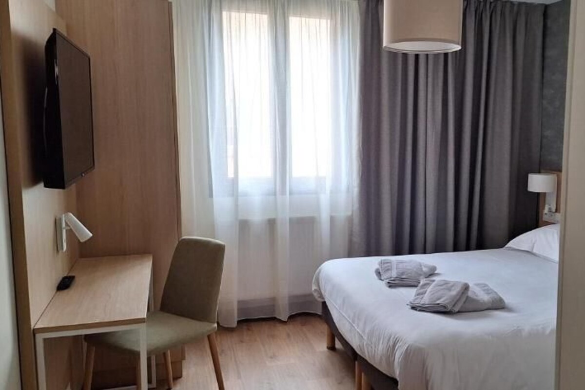A hotel room with a bed, a desk, a chair, a television, and a window with curtains.