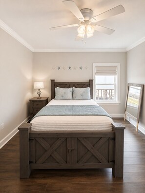 Une chambre à coucher comprenant un lit, une table de chevet, une lampe, un ventilateur de plafond et une fenêtre donnant sur un paysage agréable.