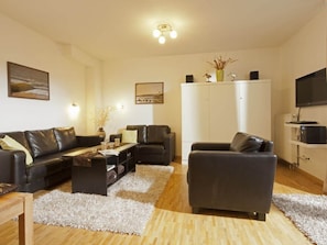 A modern living room with leather sofas, a coffee table, a white cabinet, and a television. - Holiday Apartment in Norderney With Wi-fi (Norderney)