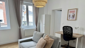 Un soggiorno moderno con un divano grigio, una sedia da ufficio nera, una scrivania in legno e un quadro appeso al muro.