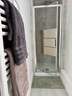 Een badkamer met een glazen douchecabine, een witte radiator en een groene mat.