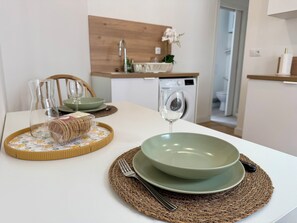 A dining table set with a green bowl, a glass, and a loaf of bread on a woven placemat. - Le Diplomate • T2 rénové au cœur de Douai (Douai)
