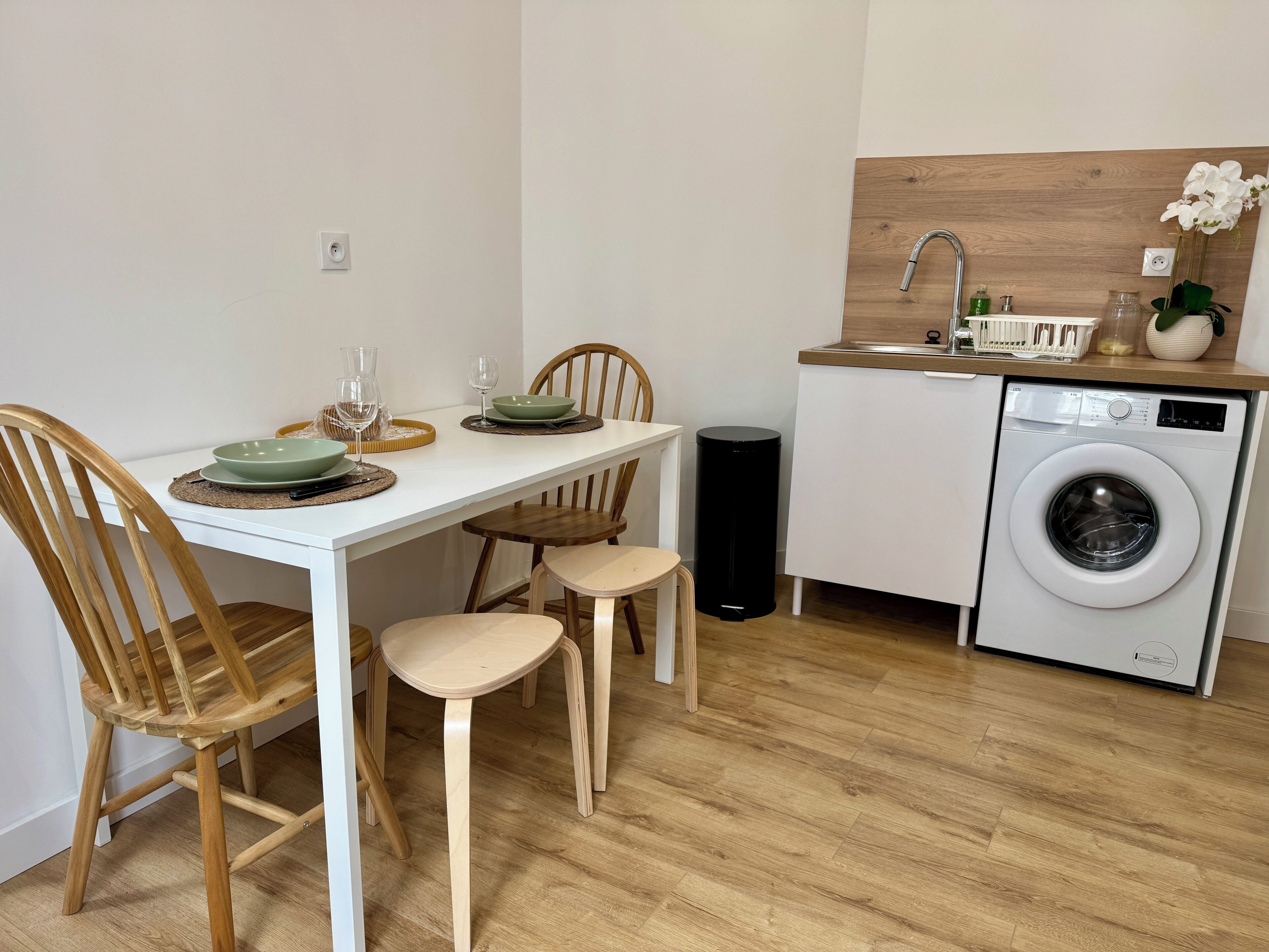 Une cuisine compacte comprenant un lave-linge, une table à manger avec des chaises et un petit coin évier.