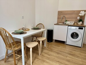 Een kleine keuken met een wasmachine, een eettafel met stoelen en een klein spoelgedeelte.