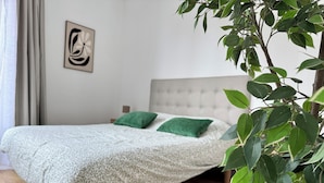 Una camera da letto con un letto, cuscini verdi, una testiera trapuntata, un'opera d'arte appesa al muro e una pianta.