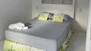 A bed with a grey mattress, white pillows, and a green bed skirt. There is a potted plant on the wall above the bed.
