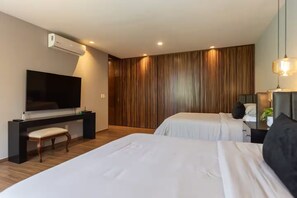 Ein Hotelzimmer mit Flachbildfernseher, Schreibtisch, zwei Betten und einer Wandpaneele aus Holz.