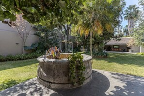 A circular concrete fountain with a water feature, surrounded by a well-maintained lawn and various plants. - Beautiful villa with a garden in the center of San Pedro Tlaquepaque, a “Pueblo Mágico”   (San Pedro Tlaquepaque)
