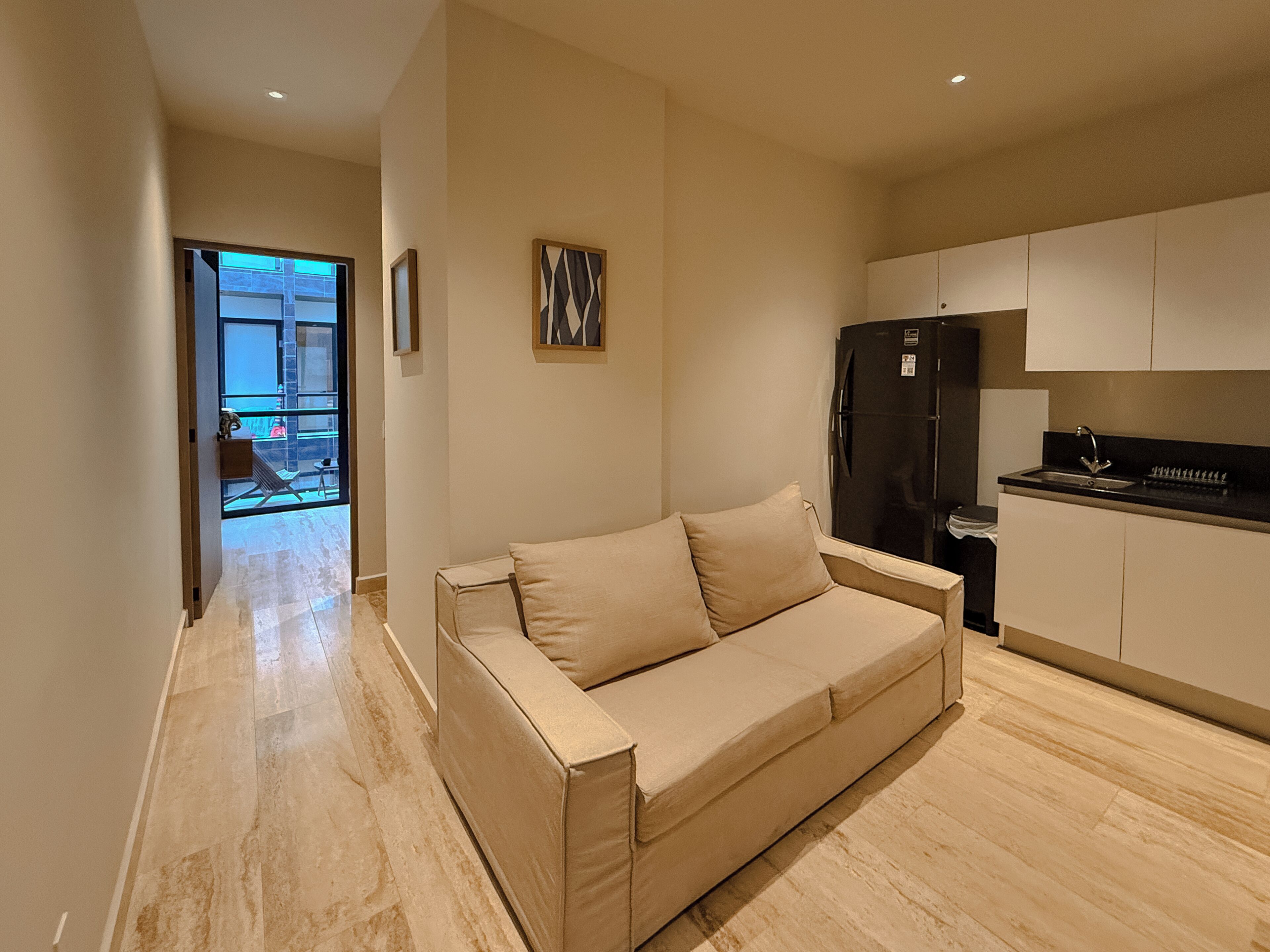 A modern living area with a beige sofa, a black refrigerator, and a kitchen with white cabinets.