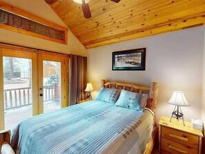 Un dormitorio con cama, dos lámparas de noche, cabecera de madera, un cuadro en la pared y una puerta corrediza de vidrio que da a un espacio al aire libre.
