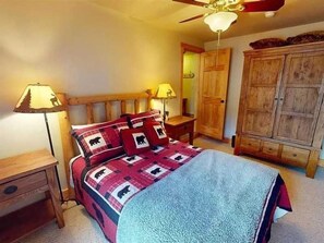 A bedroom with a bed, wooden headboard, two bedside tables, a wardrobe, and a ceiling fan.
