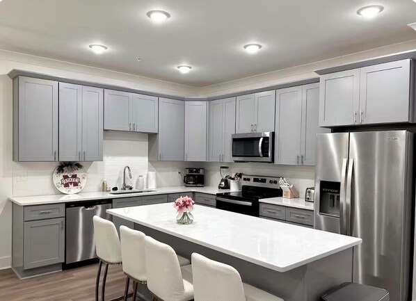 A modern kitchen with grey cabinets, stainless steel appliances, and a central island with chairs. - Starkville MS Luxury Townhome! Perfect for Gameday! 5 minutes to MSU! (Starkville)