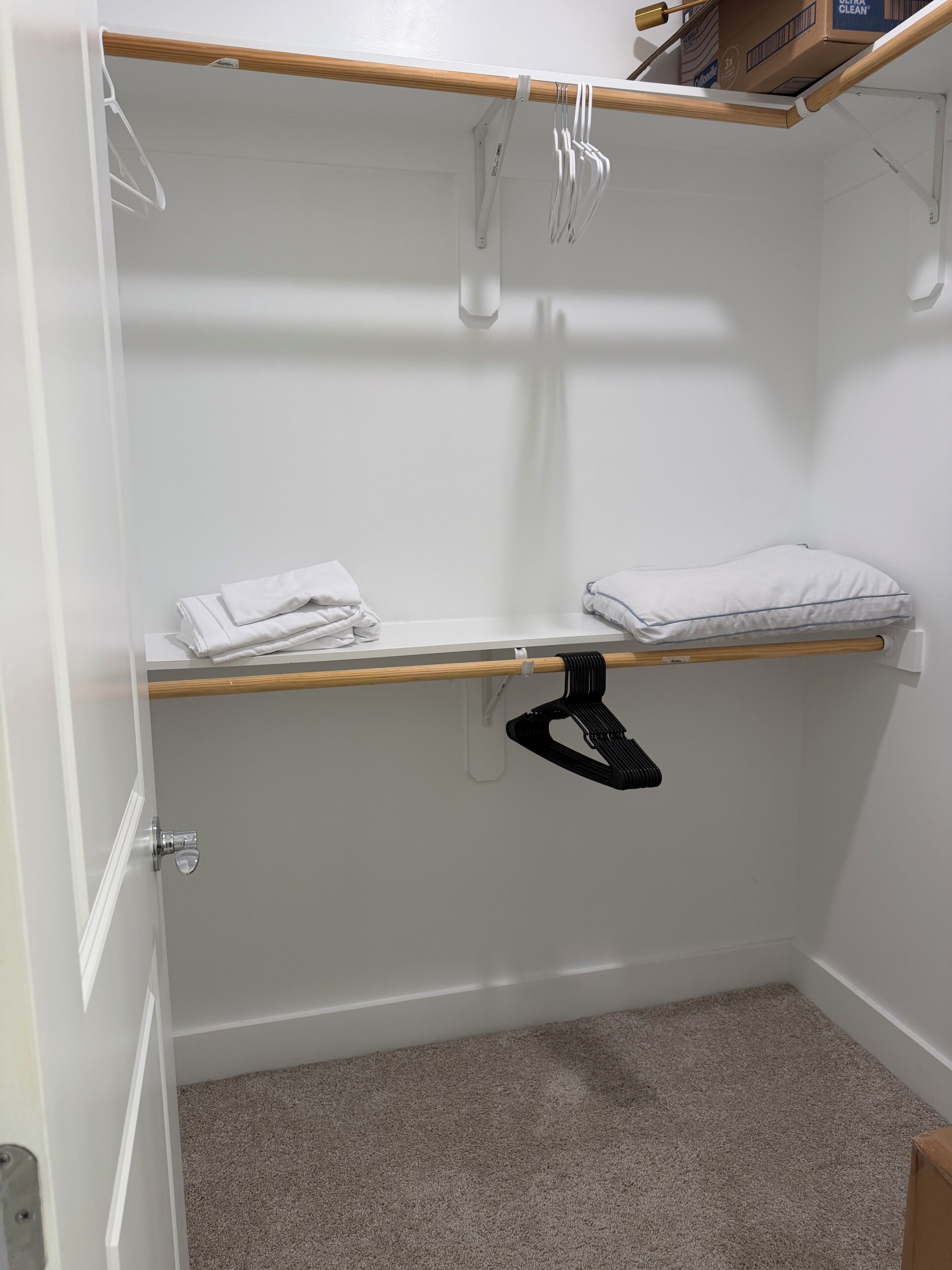 Un placard avec une tringle en bois, un porte-vêtements et une étagère où sont pliées des serviettes.