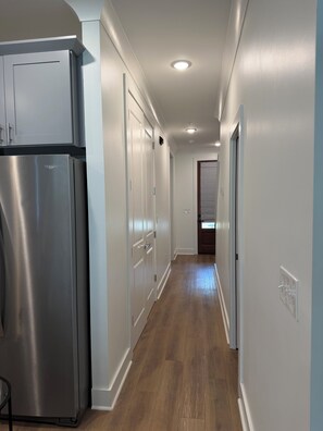 A hallway with a stainless steel refrigerator, white doors, and wooden flooring.