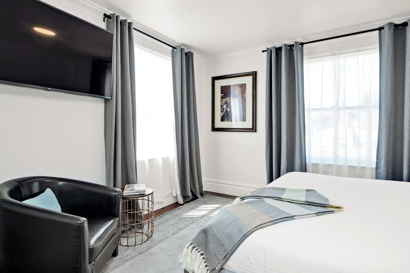 Een hotelkamer met een bed, een zwarte leren fauteuil, een klein rond tafeltje, een televisie en een lijst met een afbeelding aan de muur.