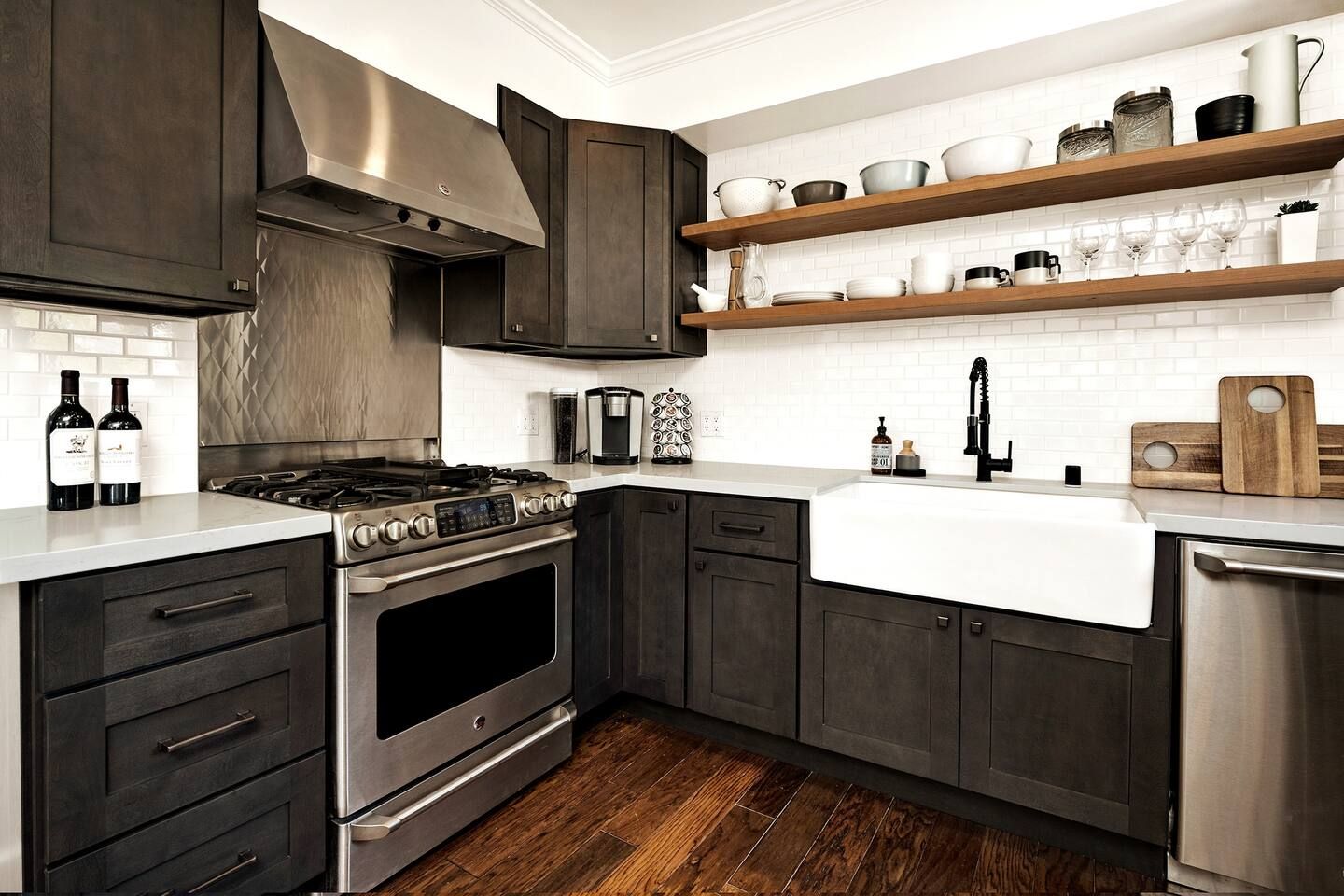 Cozinha moderna com armários escuros, eletrodomésticos de aço inoxidável e bancada branca.