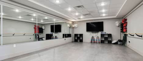 A spacious dance studio with a large mirror, ballet barres, and a television screen.